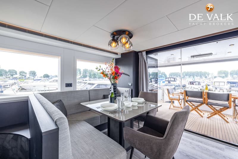 Een interieur van een boot met een eettafel, bank en stoelen, met uitzicht op een jachthaven. — Bloemsma Trawler 70
