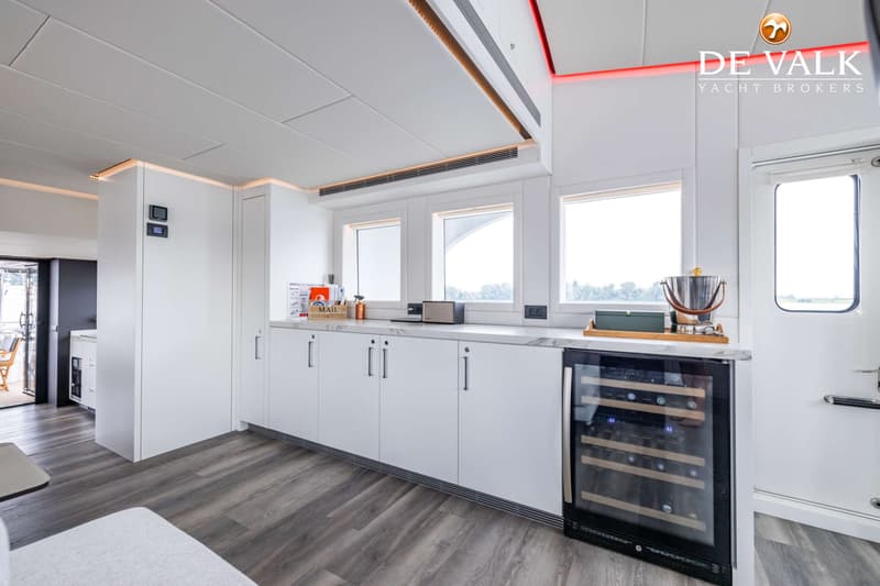 Een interieur van een boot met een witte kastenwand, marmeren aanrechtblad, drie ramen en een wijnkoeler.