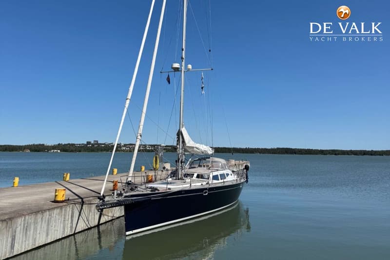 Een vrouw opent een fles champagne naast een boot die deels uit het water is getakeld, met andere boten op de achtergrond.