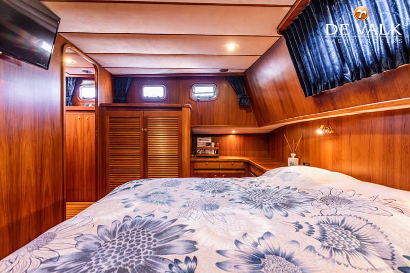 Een slaapkamer in een boot met een bed met bloemenpatroon, houten wanden en kasten, en twee patrijspoorten.