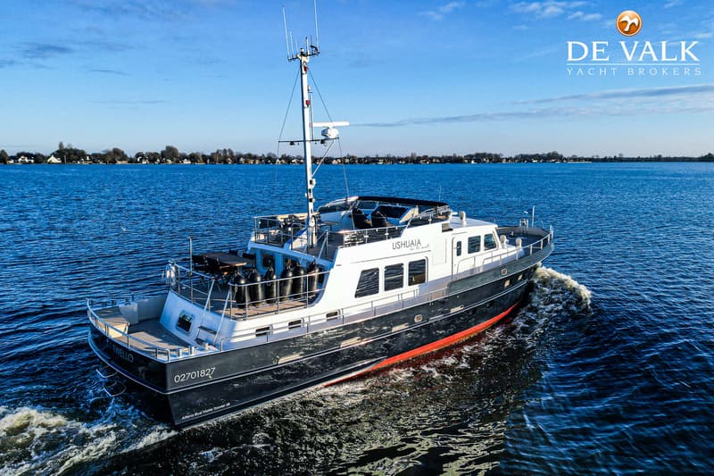 Een donkerblauwe motorboot met witte opbouw en rode onderkant vaart op een meer onder een blauwe lucht.