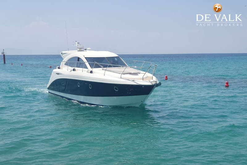 Een witte en donkerblauwe motorboot vaart op turquoise water, met boeien en een baken op de achtergrond.