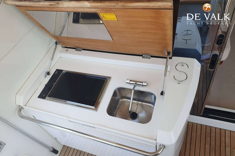 Een opengeklapte buitenkeuken met een kookplaat en een spoelbak, met een houten deksel en een spiegel.