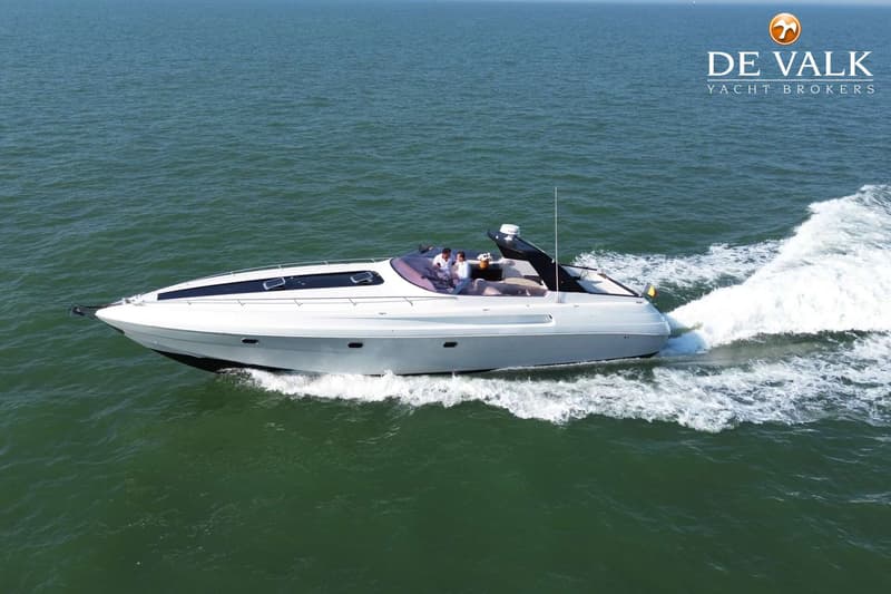 Een witte motorboot met twee personen aan boord vaart over groen water, met een kielzog achter zich.