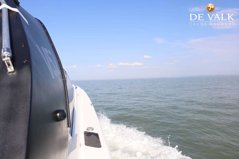 Een boot vaart over rustig water, met een witte boeg en een donkergrijze zijkant met witte letters.