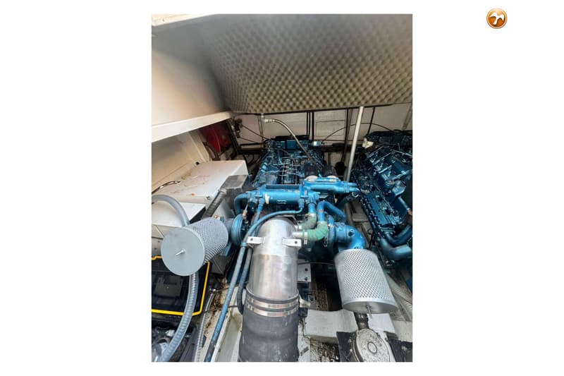 De foto toont een motorruimte met twee blauwe scheepsmotoren, omgeven door leidingen en filters.