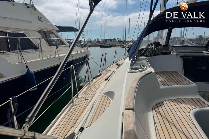 Een zeilboot met teakhouten dek ligt aangemeerd naast een grotere motorboot in een haven. — Jeanneau Sun Odyssey 54 DS