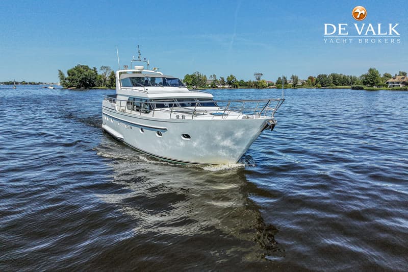 Een witte motorjacht vaart op het water met een blauwe lucht en groene oevers op de achtergrond.