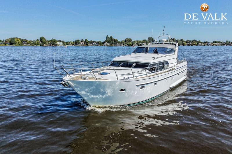 Een witte motorjacht met de naam "Harmony" vaart op blauw water onder een heldere hemel, met land in de achtergrond.