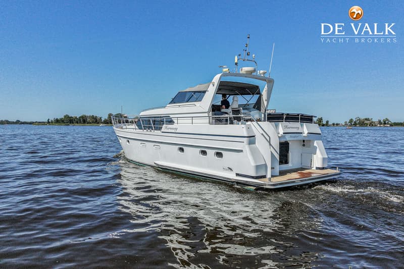Een witte motorjacht met de naam "Harmony" vaart op het water, met een persoon aan het roer.