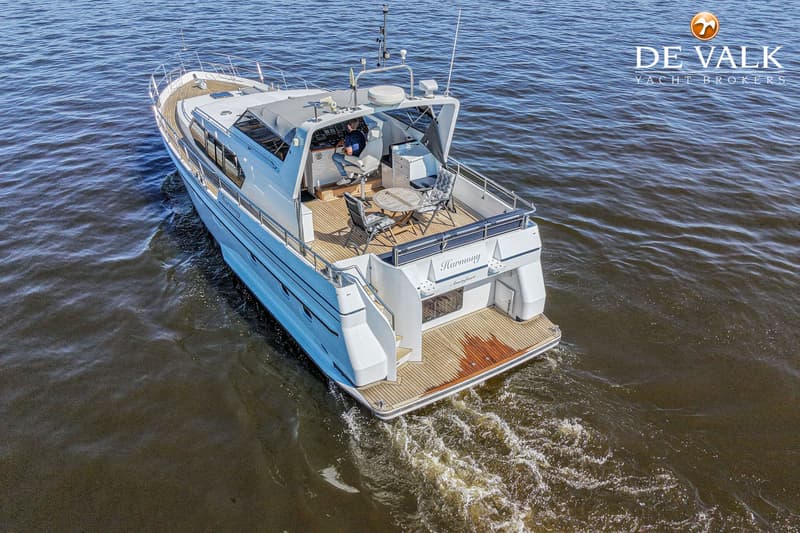 Een witte motorjacht met de naam "Harmony" op de spiegel vaart op het water, met een persoon aan het roer.