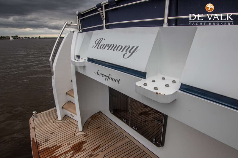 De spiegel van een boot met de namen "Harmony" en "Amersfoort" is zichtbaar, met een teakdek en een donkere waterpartij.