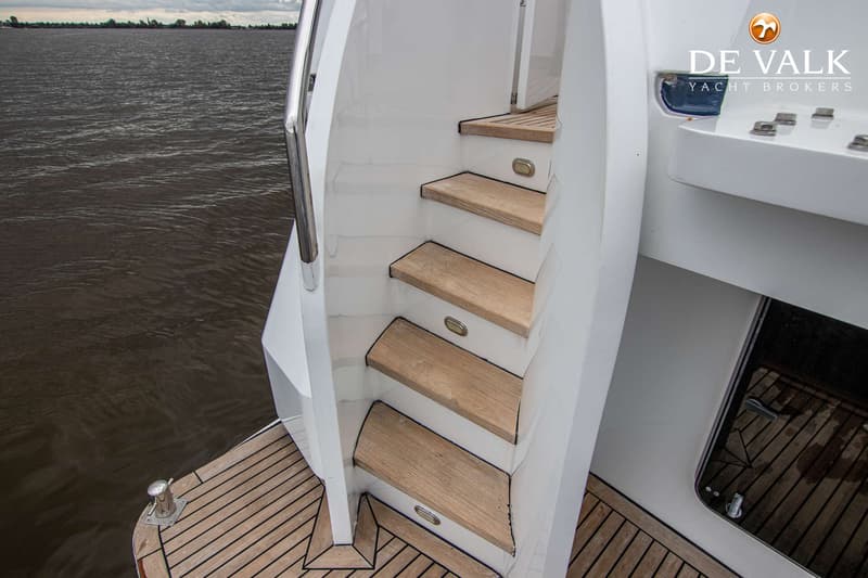 Een witte trap met houten treden en ingebouwde verlichting leidt omhoog vanaf een teakhouten dek, met donker water ernaast.
