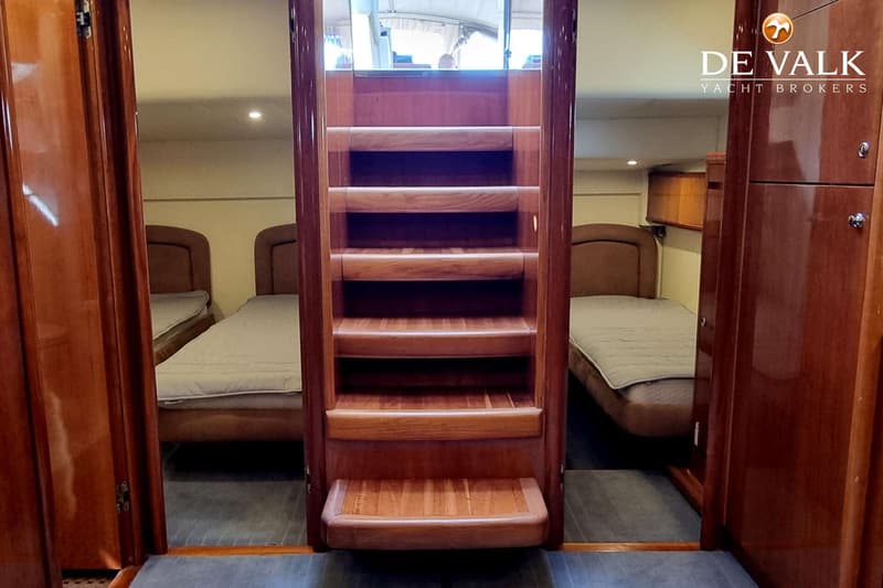 Een houten trap met vijf treden leidt naar boven, geflankeerd door twee slaapcabines met elk een bed.