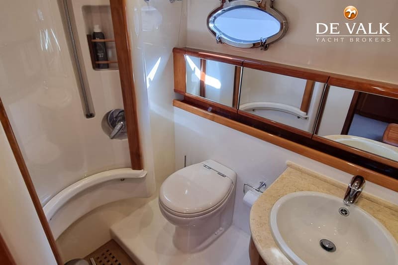 Een badkamer met een douche, toilet, wastafel en een spiegelkast, met een patrijspoort erboven.