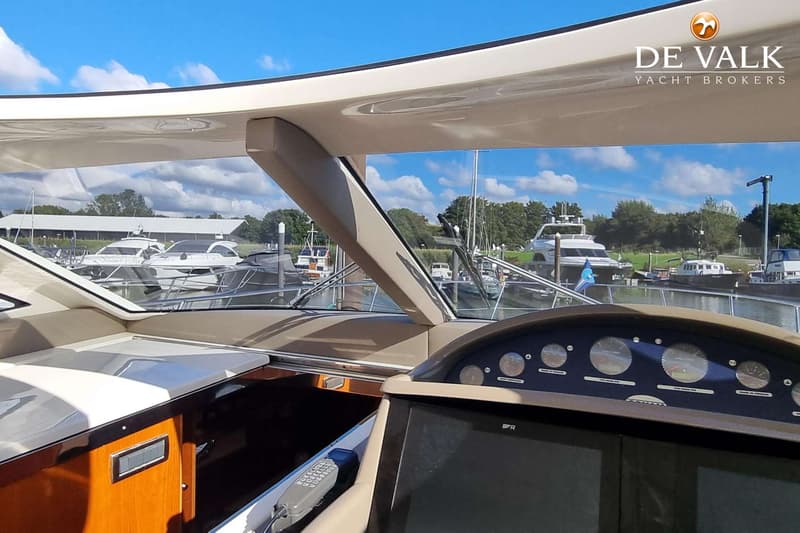 Een interieurfoto van een boot met een stuurconsole en een uitzicht op andere boten in een haven onder een blauwe lucht.