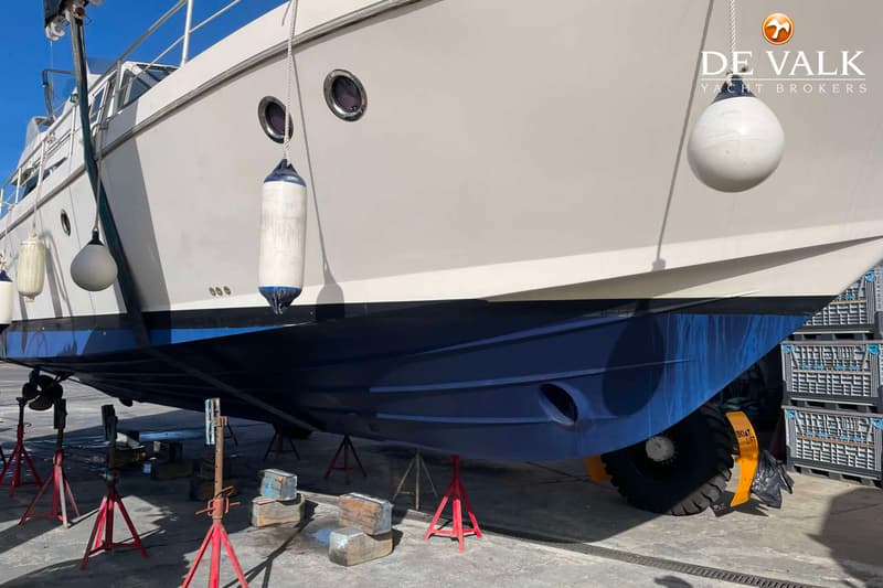 Een witte boot met een blauwe onderkant staat op rode steunen op een betonnen ondergrond. — Guy Couach 1501 Fly
