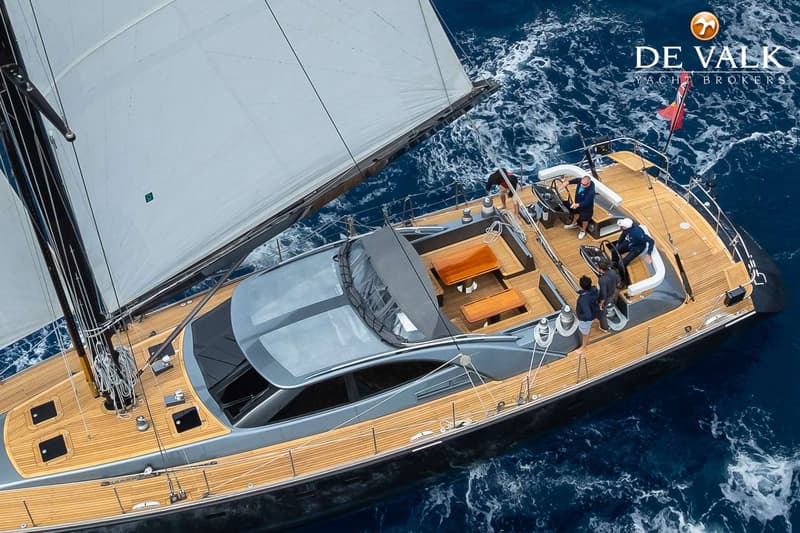 Een zeilboot met een houten dek en zeilen is te zien vanuit de lucht, met mensen aan boord. — Nordia 70 Performance Cruiser