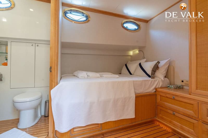 Een slaapkamer met een tweepersoonsbed, twee patrijspoorten, een toilet en houten kasten en vloer.