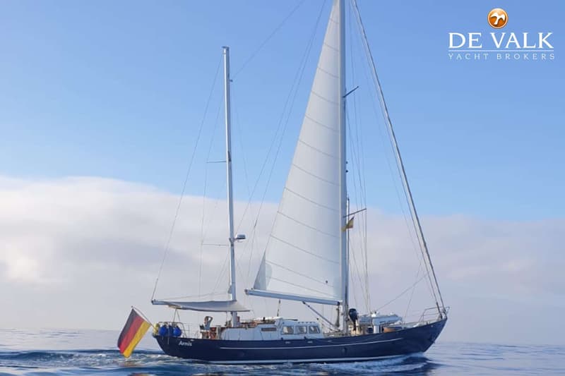 Een donkerblauwe zeilboot met twee masten en witte zeilen vaart op open water onder een blauwe lucht. — Custom Steel Ketch