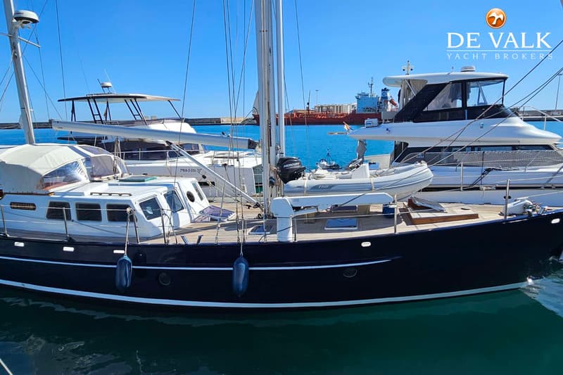 Een donkerblauwe zeilboot met een witte opbouw en een dinghy aan dek ligt in een haven. — Custom Steel Ketch