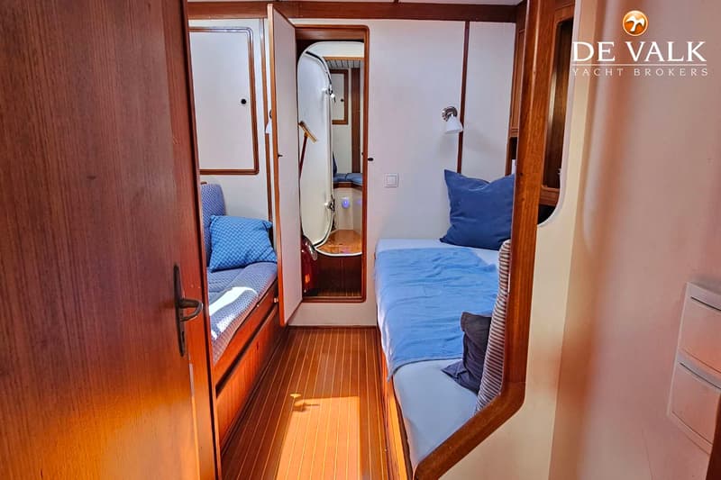 Een interieur van een boot met twee eenpersoonsbedden, een houten vloer en een open deur naar een andere ruimte.