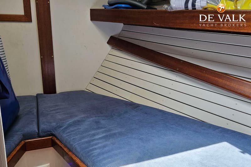 Een interieur van een boot met een blauw kussen, houten afwerking en een wit lattenpaneel. — Custom Steel Ketch
