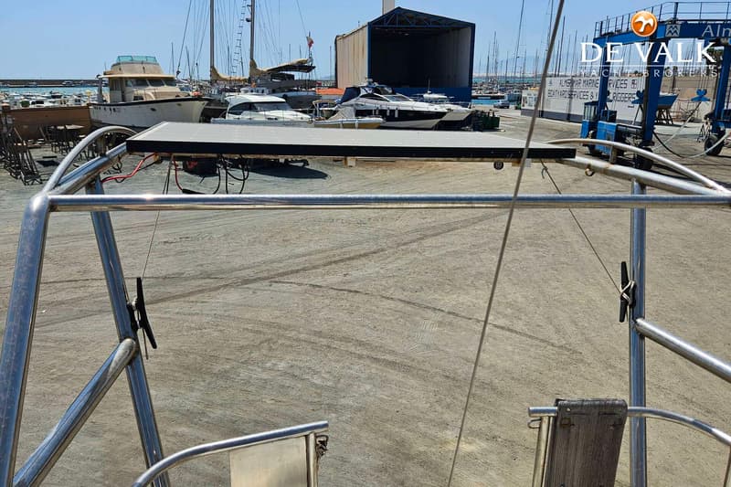Een zonnepaneel is gemonteerd op een metalen frame, met op de achtergrond een jachthaven en boten op de wal.