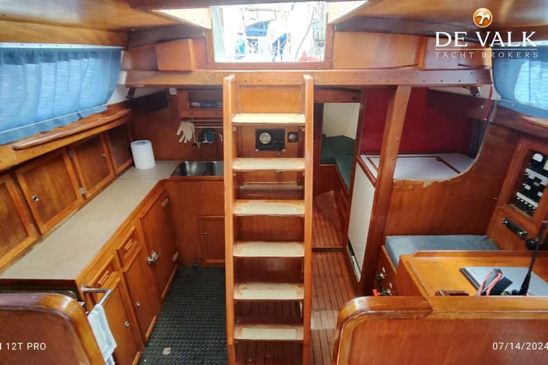 De foto toont het interieur van een boot met een houten trap, een kombuis met gootsteen en een zithoek. — Rorqual NS 44 Ketch
