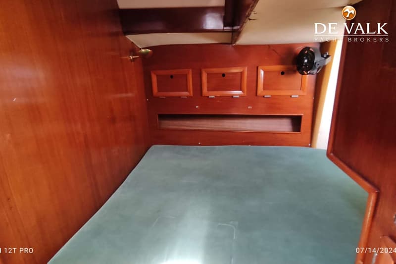 Een kajuit met een groen matras, houten wanden met opbergvakken en een lampje. — Rorqual NS 44 Ketch