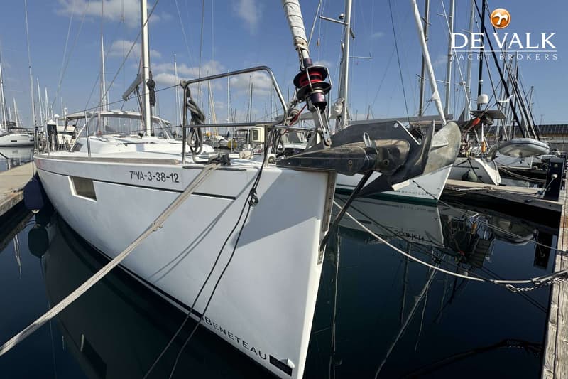 Een witte zeilboot met de registratie "7ªVA-3-38-12" ligt aangemeerd in een haven, met een anker aan de boeg.