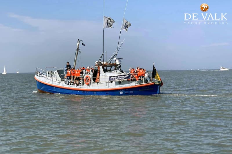 Een blauw-oranje boot met mensen in oranje reddingsvesten vaart op zee onder een heldere hemel. — Waarschip 1076 Custom