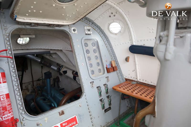 Een interieur van een boot met een open luik dat toegang geeft tot een motorruimte, een bedieningspaneel en een houten…