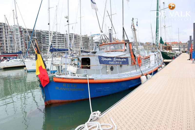 Een blauw-grijze boot met oranje accenten en een Belgische vlag ligt aangemeerd in een haven. — Waarschip 1076 Custom