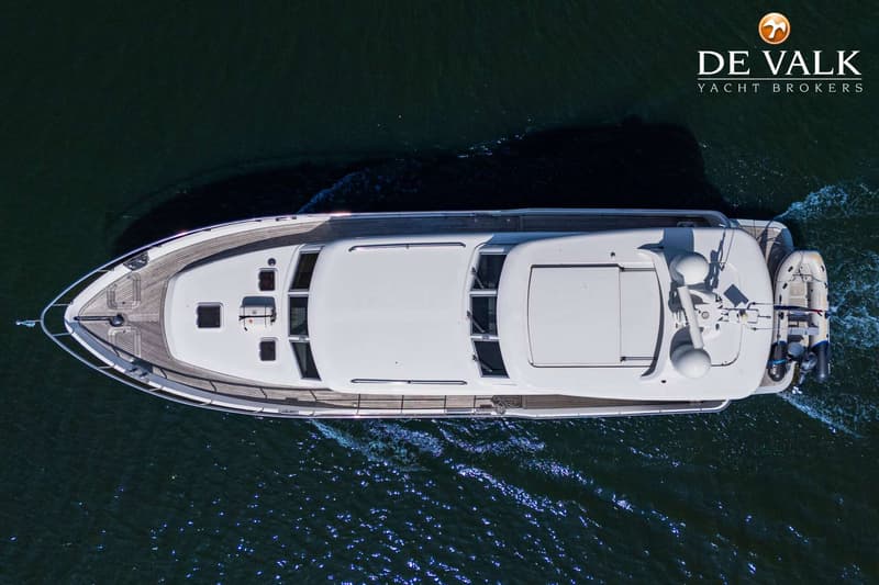 Een witte motorjacht met houten dek vaart op donkerblauw water, gezien van bovenaf.