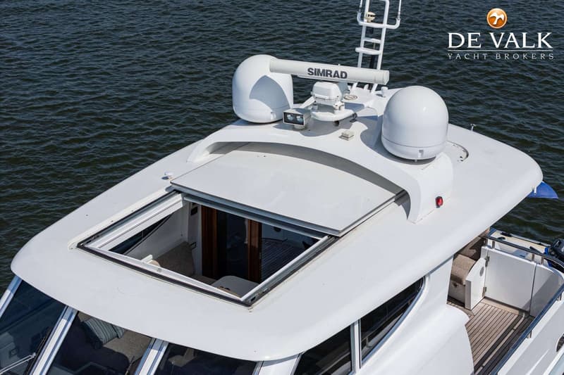 Een bovenaanzicht van een wit jacht met een open dakluik, een Simrad radar en twee witte koepels op het dak.