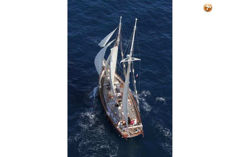Een zeilboot met twee masten en witte zeilen vaart op open water, gezien van bovenaf. — Schooner Sitting Bull 19.80