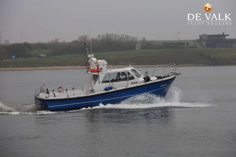Een blauw-witte motorboot vaart over water, met een landschap en gebouwen op de achtergrond. — Lochin 333 Harbour Pilot