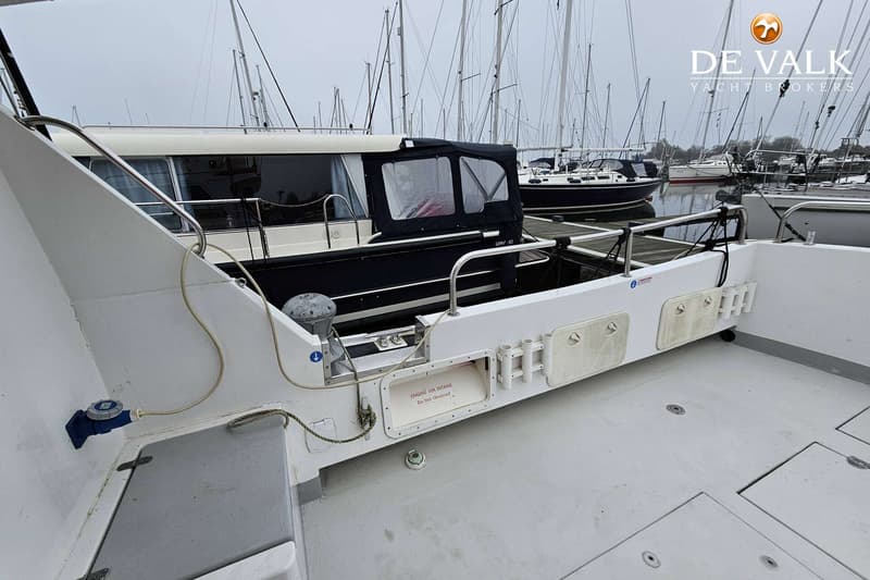 Een witte boot met een blauwe kap en een grijze vloer, met op de achtergrond andere boten in een haven.