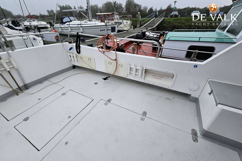 De foto toont het achterdek van een boot met luiken, een slang, hengelhouders en een motorluchtinlaat.