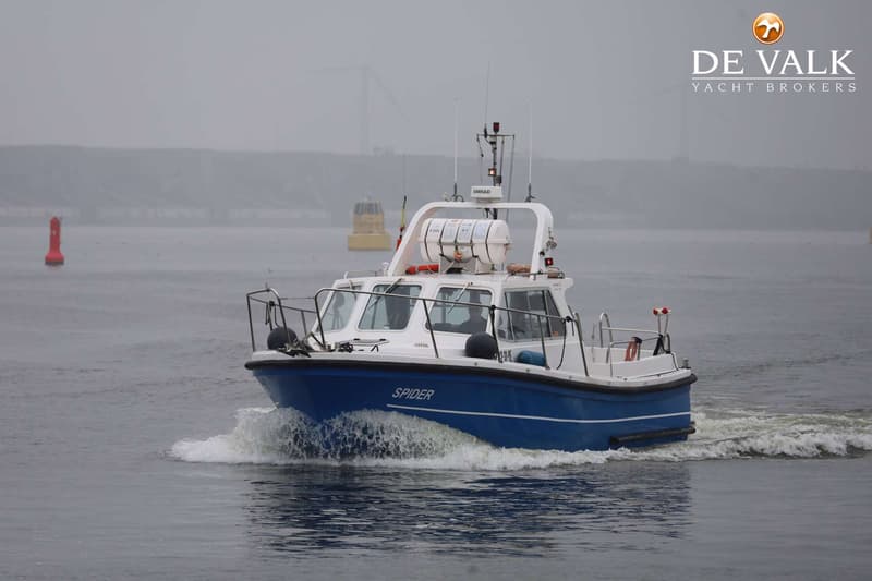 Een blauw-witte motorboot met de naam "SPIDER" vaart op water, met een rode boei en een gele boei op de achtergrond.