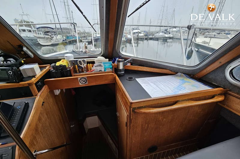 De foto toont het interieur van een boot met houten afwerking, een stuurstand, navigatieapparatuur en een zeekaart op een…