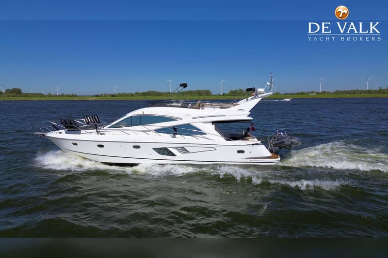 Een witte motorboot met een bijboot achterop vaart over het water, met windmolens op de achtergrond. — Galeon 530 Fly
