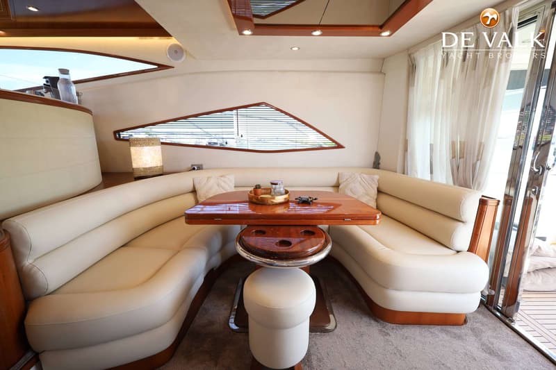 Een interieur van een boot met een U-vormige bank, een houten tafel en een krukje, met ramen en gordijnen. — Galeon 530 Fly