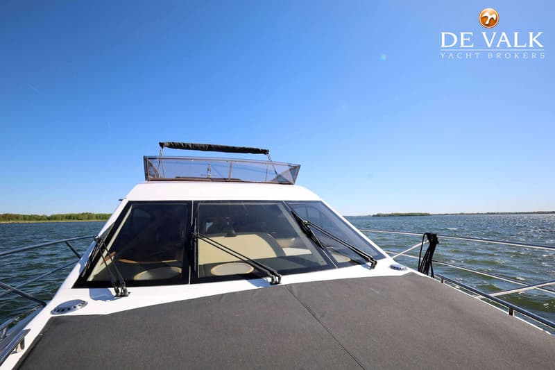 Een witte motorboot met een donkergrijze boegkap en twee ruitenwissers, varend op open water onder een helderblauwe lucht.