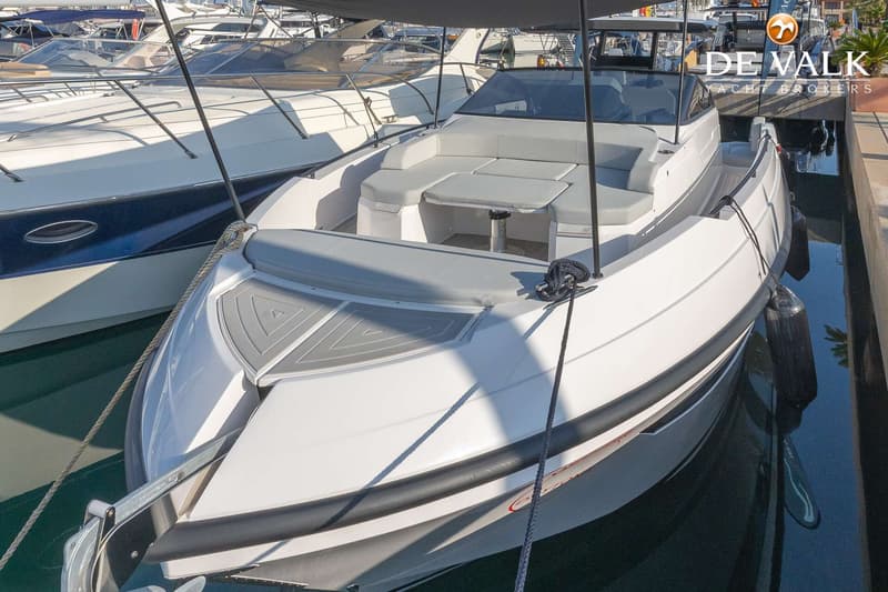 Een witte motorboot met grijze kussens en een tafel in de kuip ligt afgemeerd in een haven. — Rio Yachts Daytona 35