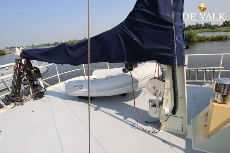 Een blauw zeil, een opblaasboot met "caribe" erop, een kraan en een lier zijn zichtbaar op het dek van een boot.