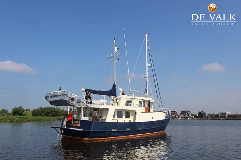 Een blauw-witte motorboot met twee masten en een bijboot hangend aan davits, drijft op rustig water.