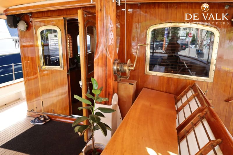 Een houten bootinterieur met een open deur, ramen, een plant en een lier.