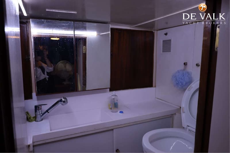 Een badkamer aan boord van een boot met een wastafel, kraan, spiegelkast, toilet en een blauwe douchespons.